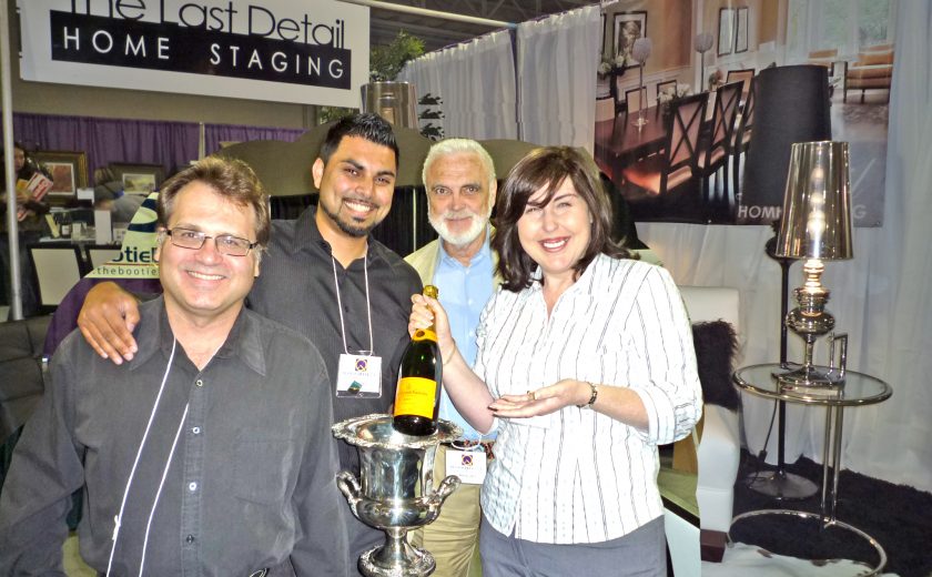 ella wins champagne, three men standing with woman, white curtains and staging lamps in the background