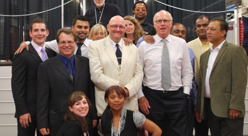 The All Canadian Self Storage Team, group of over 10 people standing, black curtain background