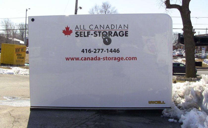 white storage unit sitting on parking lot, white snow, brown tree, buildings in the background