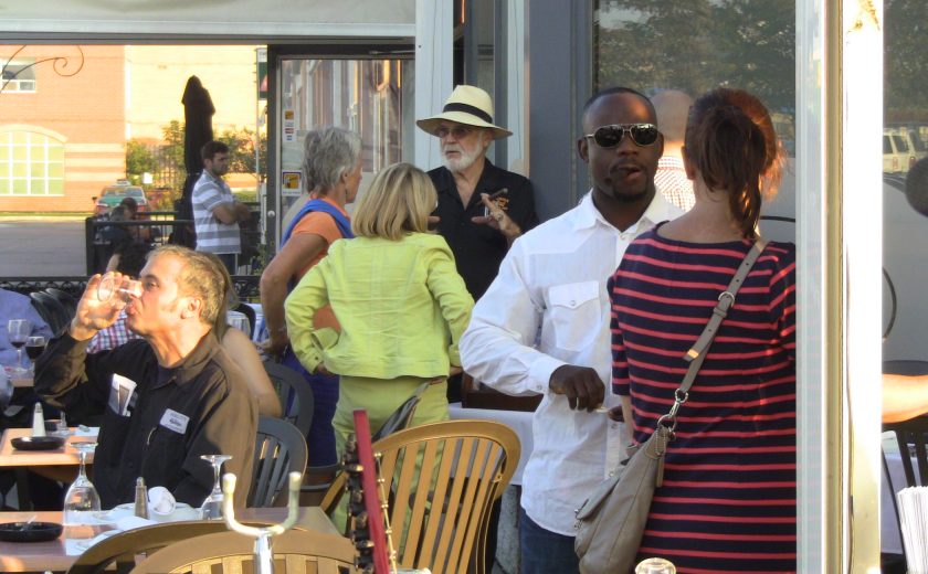 group of people on the patio talking outside, brown and black tables and chairs