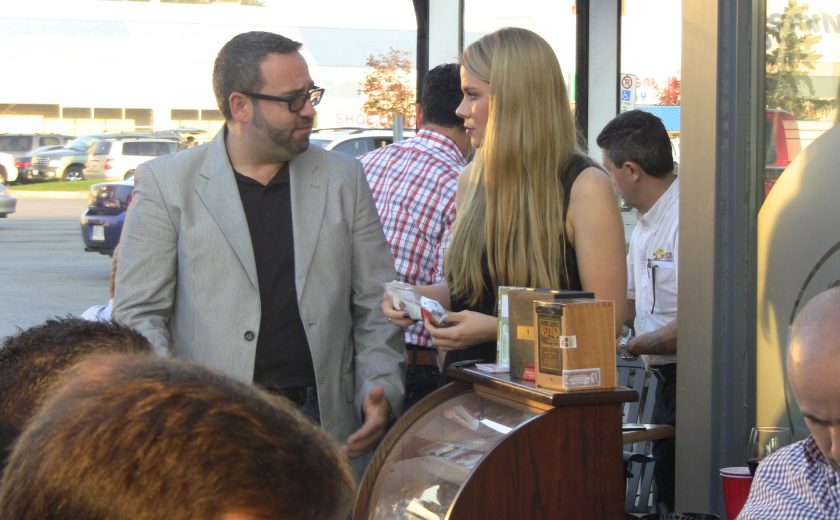 woman with long blonde hair talking to man wearing a grey suit and black dress shirt, outside on a patio