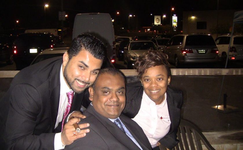 group of three people smiling, dark night sky, parking lot full of cars in the back