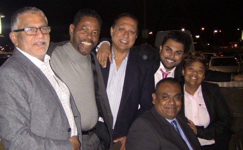 group of 6 wearing dress shirts and tuxes, dark night sky, parking lot full of cars behind them