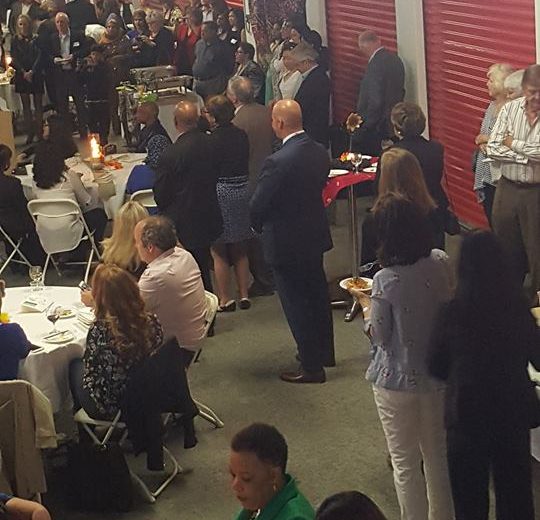 Flavours of Thorncliffe, large group of people inside storage facility eating at round tables, red storage units in the back