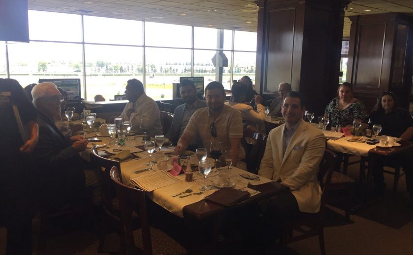 Woodbine Races, group photo of everyone sitting at the tables, brown chairs and tables, bright large window in the background