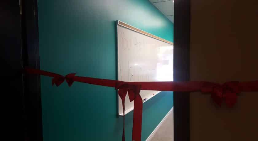 long red ribbon with three bows across open client management office door, teal coloured wall with whiteboard hanging