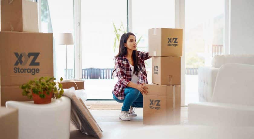 young woman wearing a plaid shirt with blue jeans and white shoes, packing her belongings using XYZ Storage boxes