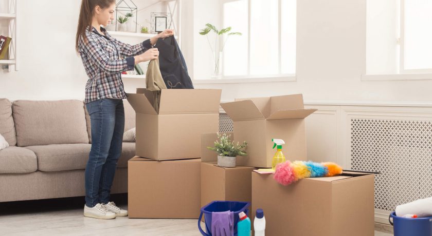 lady wearing plaid shirt and blue jeans packing belongings in brown boxes in white room