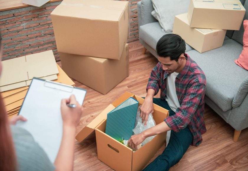 Young Asian couple packing their belonging into cardboard box by using a check list before moving to new resident or house after buy or rent a new one.