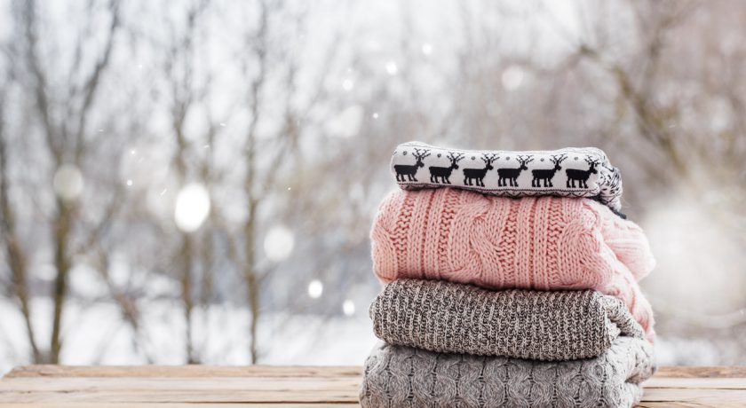 Stack of knitted sweaters on wooden tableon winter nature background.