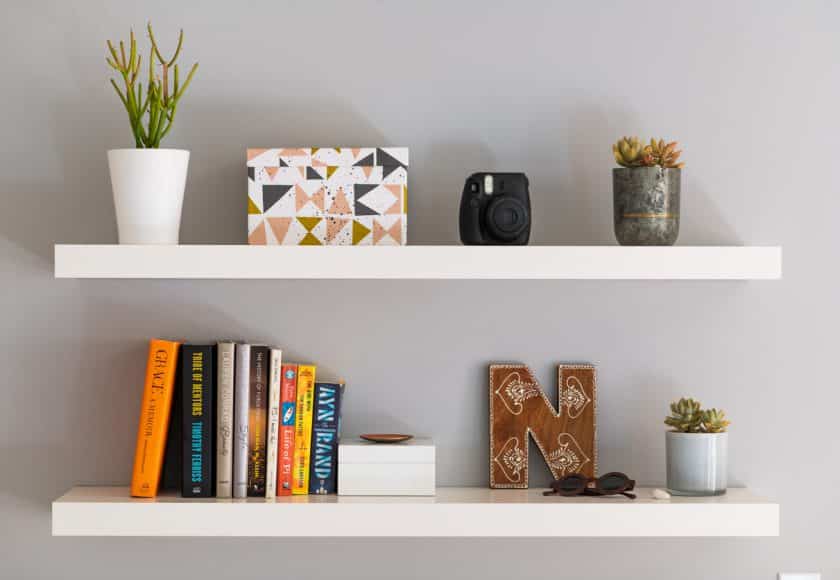 Two white painted modern bookshelves with books, plants, a decorative storage box and personal items.