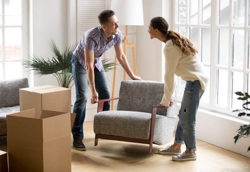 Smiling couple carrying modern chair together placing furniture moving into new home, young family discussing house improvement interior design while furnishing living room, remodeling and renovation