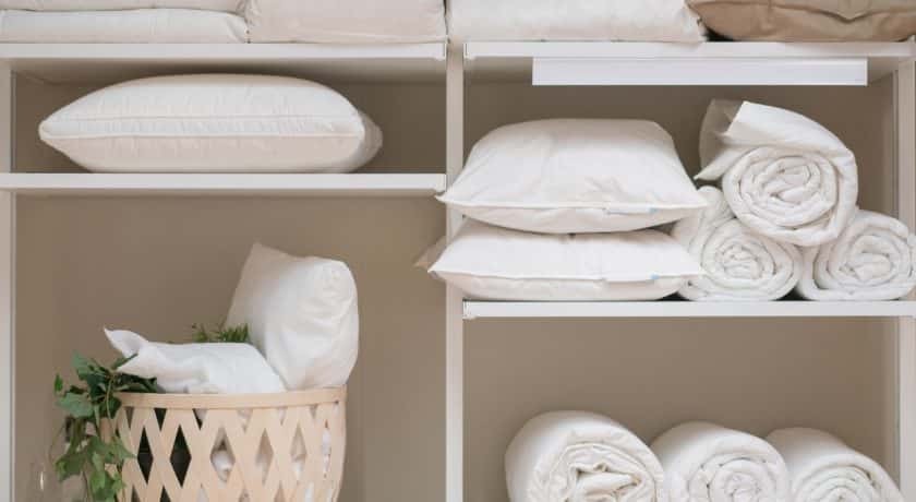 Various household items such as pillows and quilts standing in the white cupboard in the laundry room.