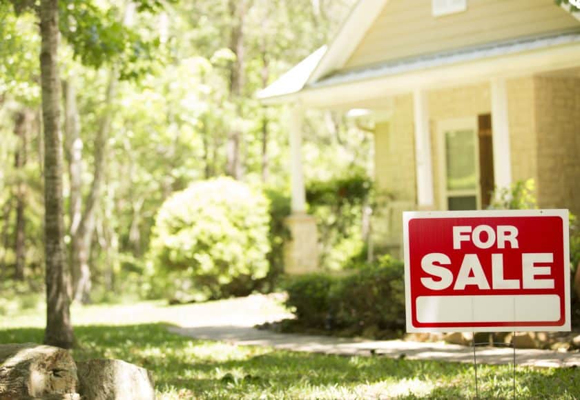 Home for sale with real estate sign in spring or summer season.